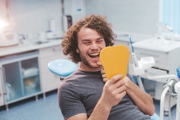 Young man looking at his smile in a yellow mirror during dental visit