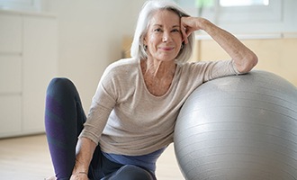 Woman smiling while resting on yoga ball in workout room