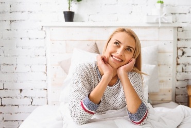 Woman sitting in bed and smiling while daydreaming
