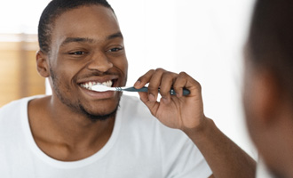 Man smiling while brushing his teeth in bathroom