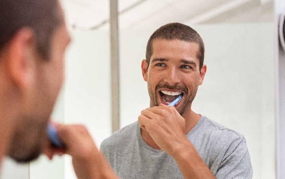 Man smiling while brushing his teeth in bathroom