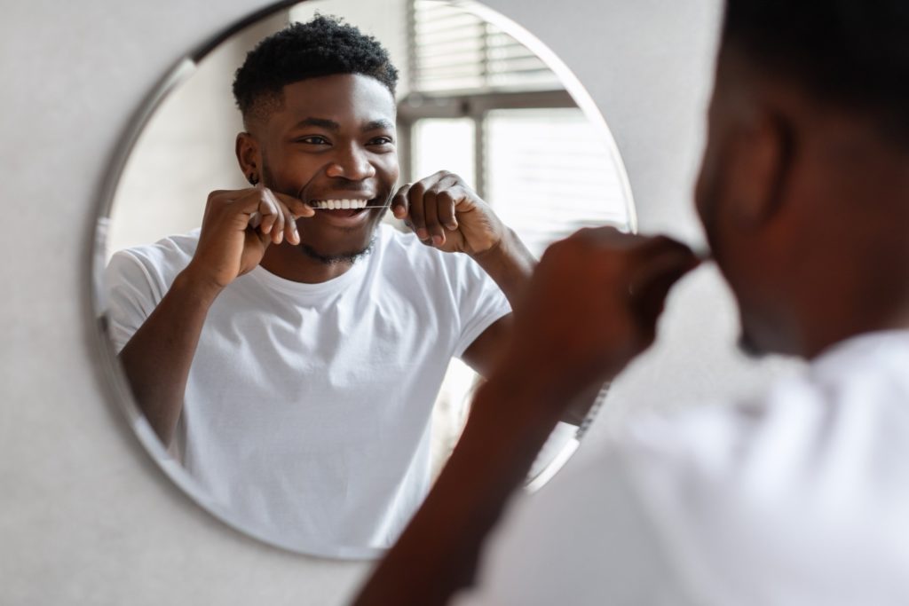 Man smiling at reflection while flossing his teeth